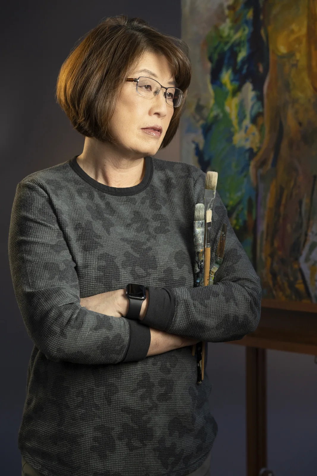 Editorial portrait of a painter holding brushes in front of one of her own canvases