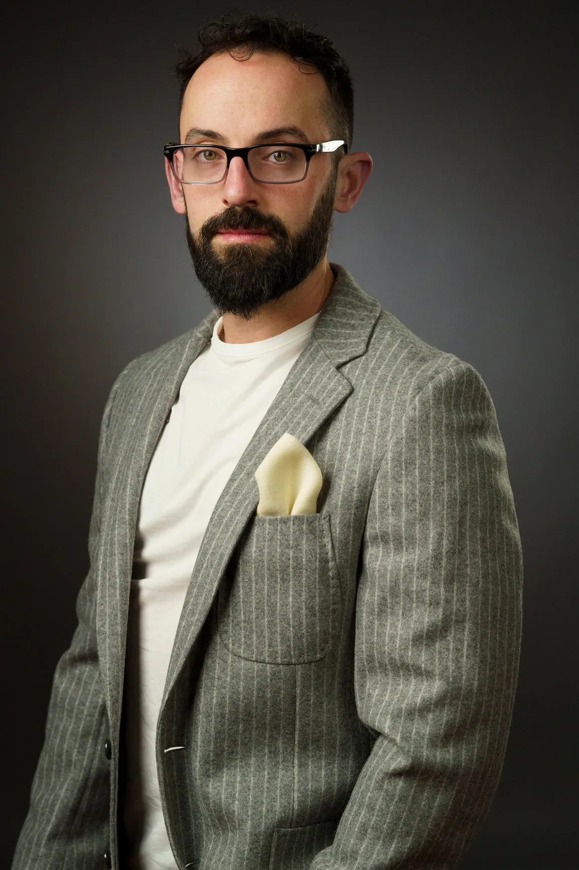 Studio headshot of a bearded man in glasses and a gray flannel jacket with clean, matte skin